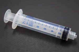 A clear plastic syringe with measurement markings on a gray background.